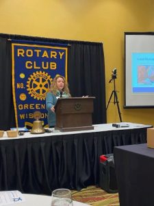 A woman talks at the podium of a Rotary Club meeting, the Rotary Club banner is behind her.