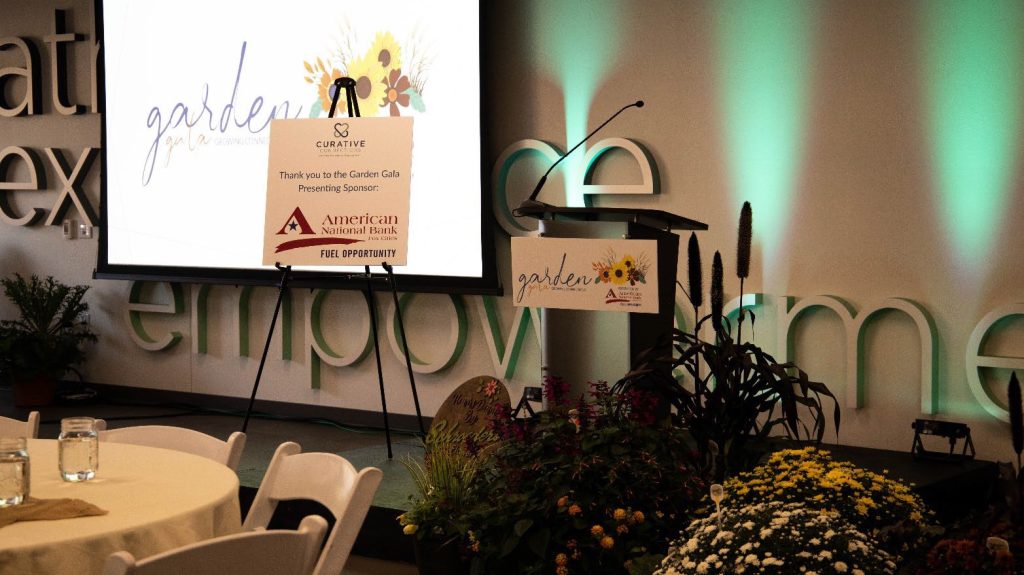 The front of the room for the 2023 Garden Gala fundraiser event, featuring a podium surrounded by flowers.
