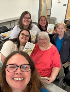 Six members of the Curative Connections' Diversity, Equity, Inclusion, and Belonging Committee take a selfie with the book Maid: Hard Work, Low Pay, and a Mother's Will to Survive by Stephanie Land.