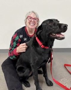 Photo of Ellen Conley posing with her black labrador dog