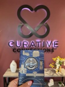 A photo of the My Draft Experience booklet in front of a Curative Connections sign on a wall.