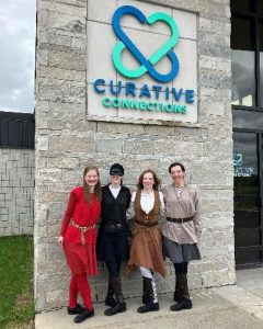 The four members of Treble Alliance posing in front of the Curative Connections sign.